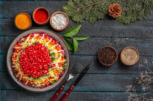 Top view tasty food appetizing Christmas food and bowls of spices next to the fork knife spruce branches with cones