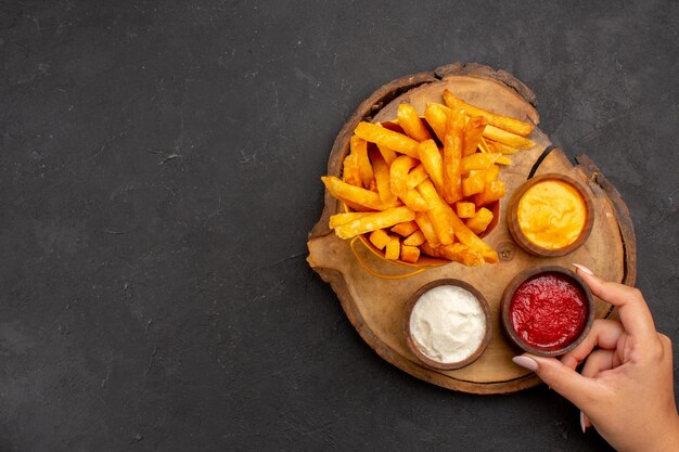 Top view of tasty french fries with different sauces on black