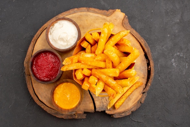 Top view of tasty french fries with sauces on dark