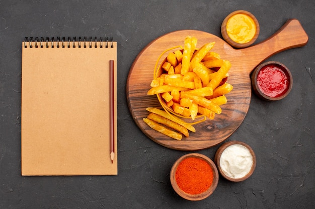 Top view of tasty french fries with sauces on dark