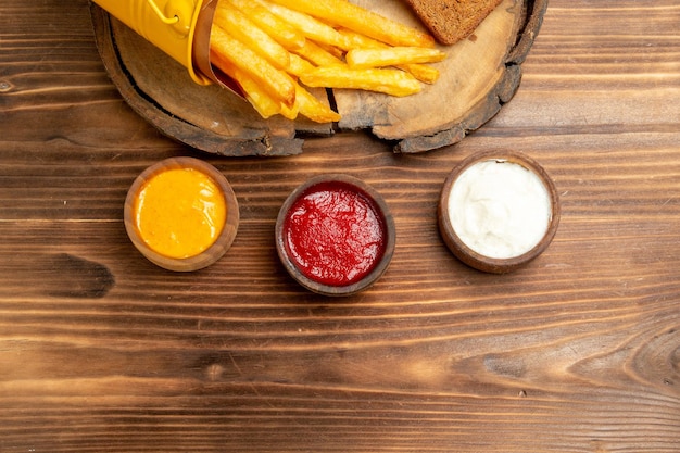 Top view of tasty french fries with seasonings on brown table