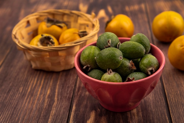 Top view of tasty fresh feijoas on a bowl with persimmon fruits on a bucket on a wooden surface