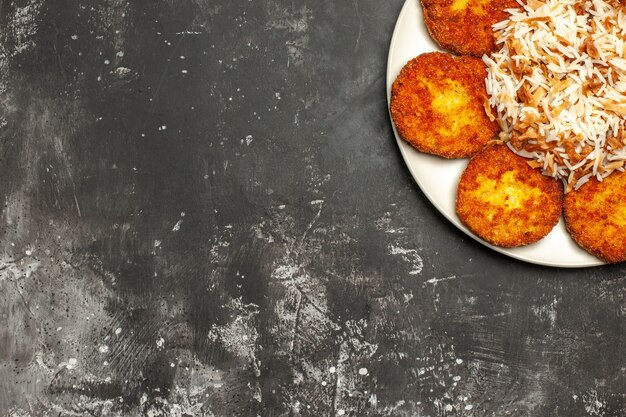 Top view tasty fried cutlets with cooked rice on a dark surface photo meat dish meal