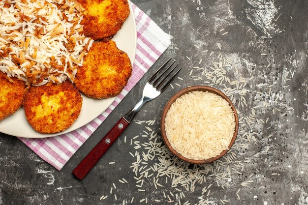 Top view tasty fried cutlets with cooked rice on dark surface rissole meat dish