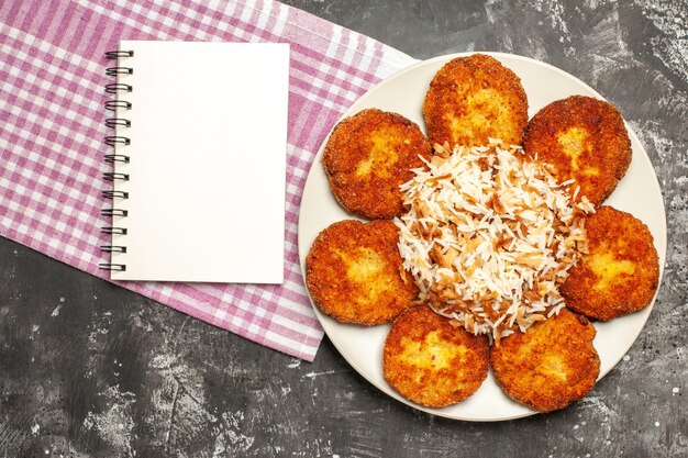 Top view tasty fried cutlets with cooked rice on a dark surface rissole meat food