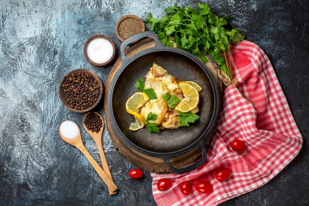 Top view tasty fried fish with lemon and parsley in pan on wood board