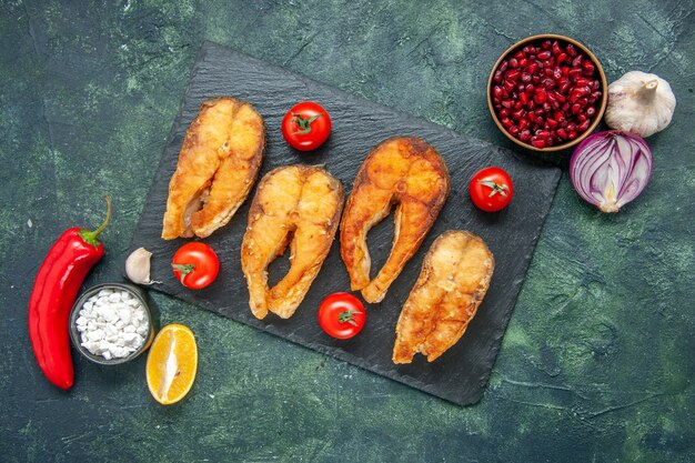 Top view of tasty fried fish with red tomatoes, garlic, lemon and red pepper