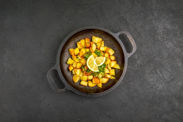 Foto gratuita vista dall'alto di gustose patate fritte all'interno della padella con fette di limone sulla superficie scura