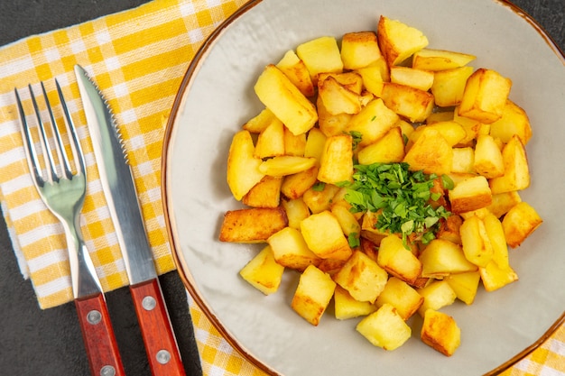 Вид сверху вкусного жареного картофеля внутри тарелки на темно-серой поверхности