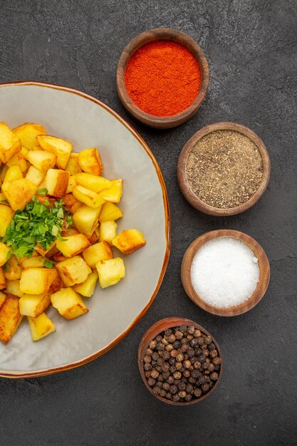 Foto gratuita vista dall'alto di gustose patate fritte all'interno del piatto con condimenti sulla superficie scura