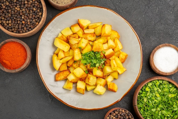 Vista dall'alto di gustose patate fritte all'interno del piatto con condimenti sulla superficie scura