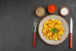 Foto gratuita vista dall'alto di gustose patate fritte all'interno del piatto con condimenti sulla superficie scura