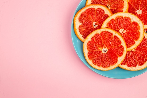 Вид сверху вкусных кусочков фруктов грейпфрутов внутри тарелки на розовой поверхности