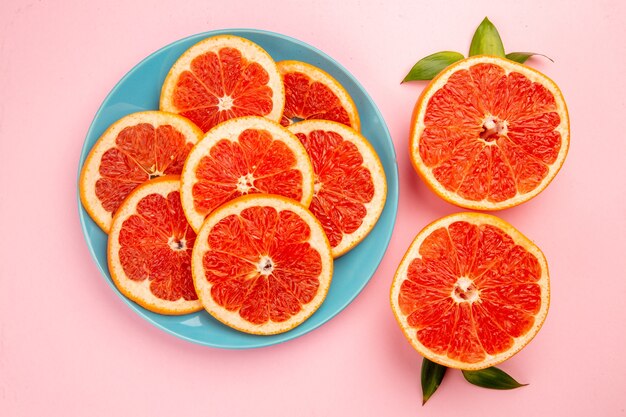 Top view of tasty grapefruits fruit slices inside plate on pink surface