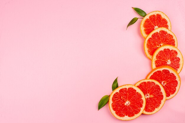 Top view of tasty grapefruits juicy fruit slices on pink surface