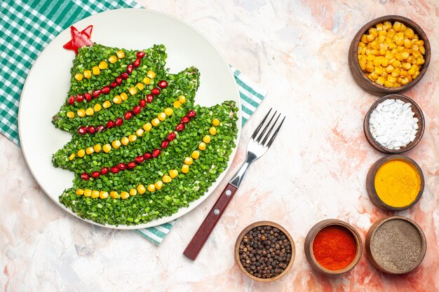 Top view tasty green salad in new year tree shape with seasonings on a light background