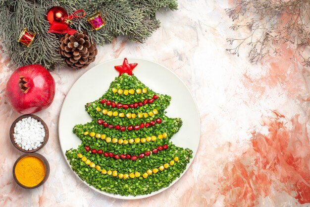 Вид сверху вкусный зеленый салат в форме новогодней елки с приправами на светлом фоне