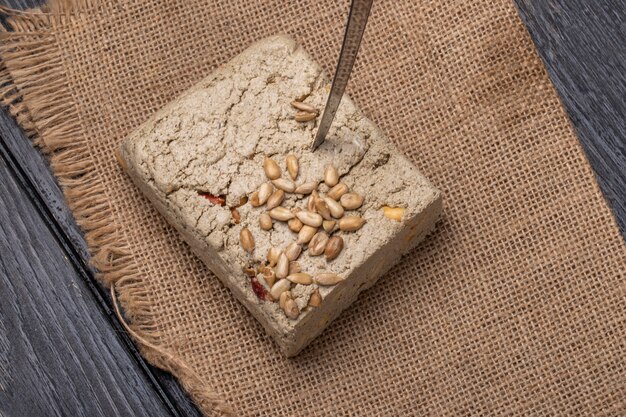 Top view of tasty halva with a knife and sunflower seeds on a sackcloth