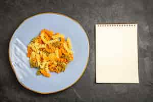 Foto gratuita vista dall'alto gustosa pasta italiana insolita pasta cotta a spirale sulla scrivania scura