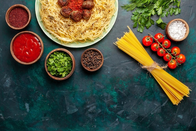 Вид сверху вкусной итальянской пасты с фрикадельками и разными приправами на темно-синем фоне