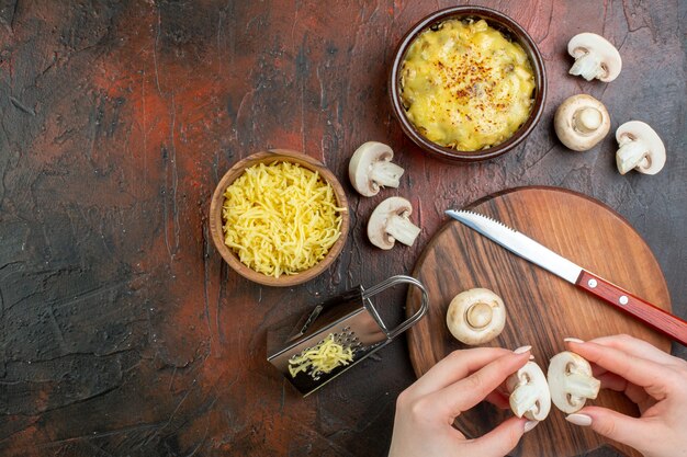 Top view tasty julienne in bowl grater cut mushrooms in female hands knife on cutting board grated mosarella in bowl on brown table