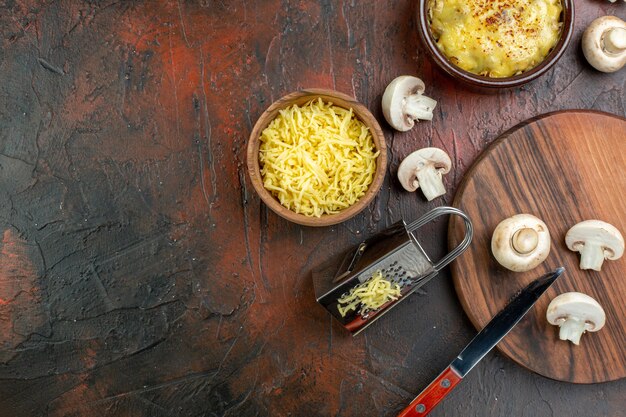 Top view tasty julienne in bowl grater mushrooms and knife on cutting board grated mosarella in bowl on brown table