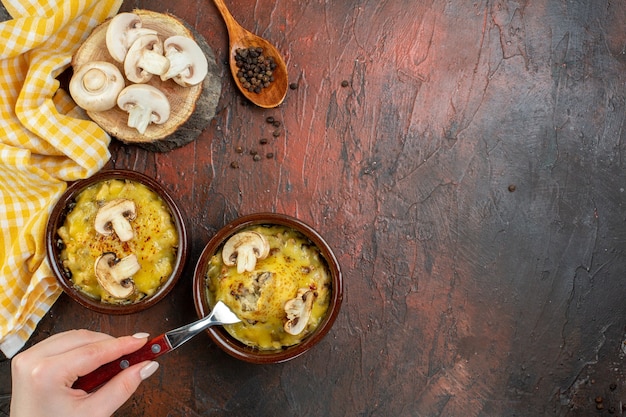 Top view tasty julienne in bowls fork in female hand black pepper in wooden spoon on dark red table