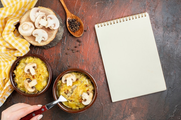 Top view tasty julienne in bowls fork in female hand notepad wooden spoon on dark red table