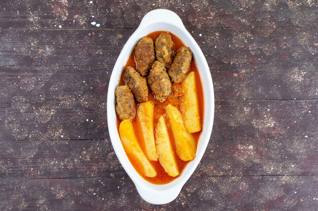 Вид сверху вкусные мясные котлеты, приготовленные вместе с картофелем и соусом внутри тарелки на коричневом фоне, блюдо из мяса и картофеля, ужин
