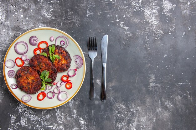 灰色の床の食事料理の写真にオニオンリングが付いた上面図のおいしい肉カツレツ