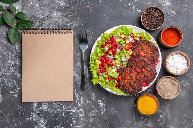 Vista dall'alto gustose cotolette di carne con insalata e condimenti su sfondo grigio foto piatto di cibo