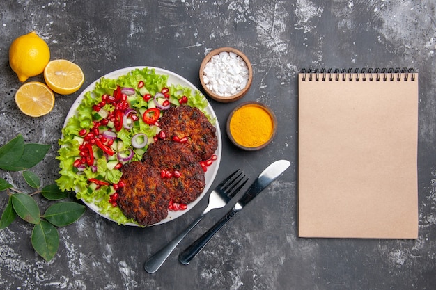 Vista dall'alto gustose cotolette di carne con insalata e condimenti sul piatto di cibo foto pavimento grigio