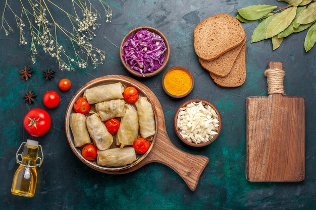 Top view tasty meat meal rolled with cabbage and tomatoes called dolma with olive oil and bread on dark-blue desk