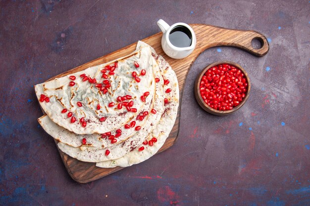 Top view tasty meat qutabs pitas with fresh red pomegranates on dark-purple surface food meat dough pita