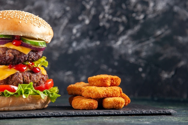 Top view of tasty meat sandwich on dark color tray and chicken nuggets on black surface