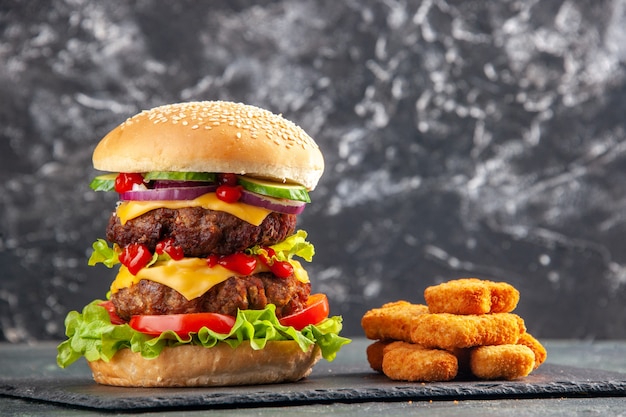 Top view of tasty meat sandwich with tomatoes green on dark color tray and chicken nuggets on black surface