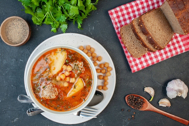 Вид сверху вкусный мясной суп с темными буханками хлеба на темном фоне