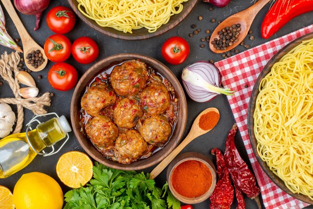 Top view tasty meatball soup in bowl spaghetti in bowl oil bottle tomatoes parsley on table