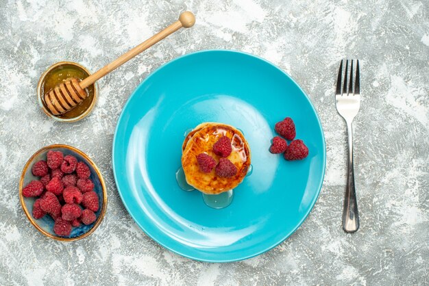 Top view of tasty muffins with berries and honey on light surface