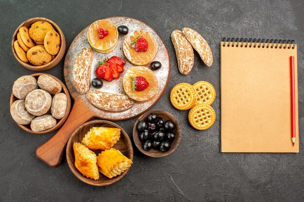 Top view tasty pancakes with different sweets on dark desk sugar cake dessert