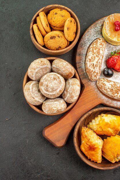 Top view tasty pancakes with different sweets on the dark surface sugar cake dessert