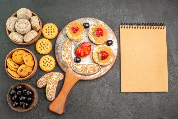 Top view tasty pancakes with sweet cakes and fruits on dark desk