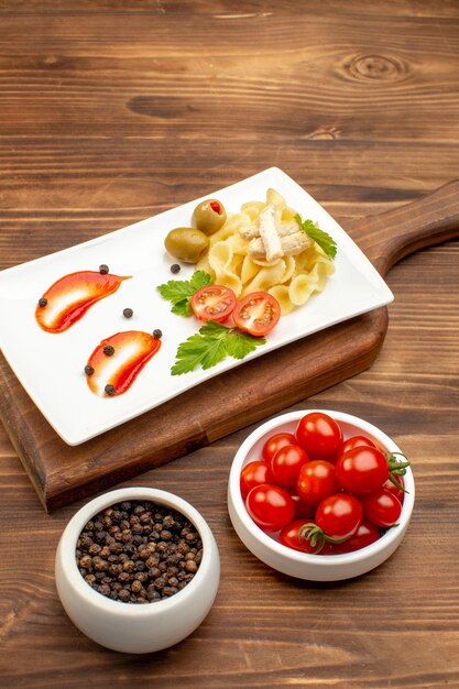 갈색 나무 표면에 있는 커팅 보드 고추 토마토에 흰색 접시에 야채와 함께 제공되는 맛있는 파스타 식사의 상위 뷰