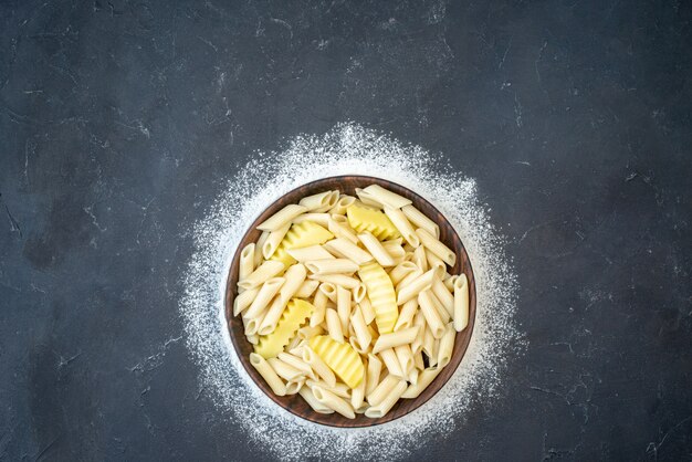 Top view tasty penne pasta with potato in bowl sprinkled flour on black table copy place