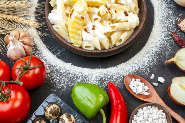 Вид сверху вкусной пасты пенне с картофелем в миске, помидорами, чесноком, перцем, морской солью на столе