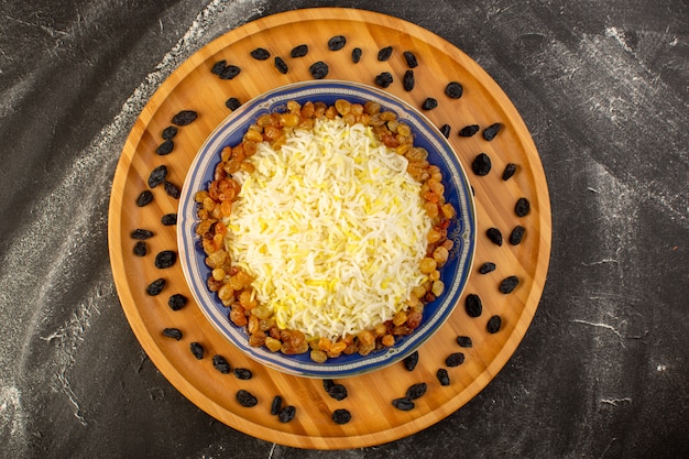 Вид сверху вкусного плова с маслом и изюмом внутри тарелки на темной поверхности