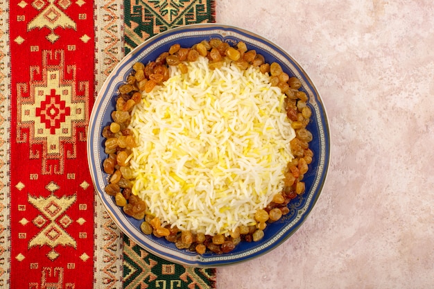 A top view tasty pilaf with oil and dried raisins inside plate on the pink surface