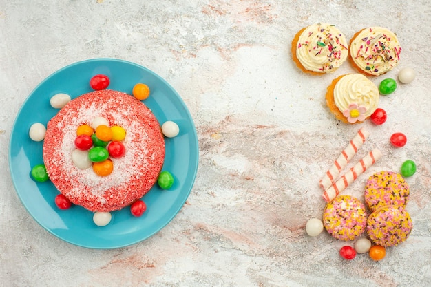 Foto gratuita vista dall'alto gustosa torta rosa con biscotti su superficie bianca goodie arcobaleno caramelle dessert color cake