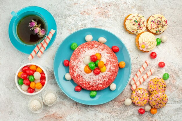 Top view tasty pink cake with yummy cookie cakes and tea on white surface goodie rainbow candy dessert color cake