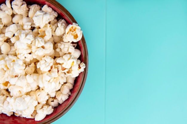 Top view of tasty popcorn on a wooden bowl on blue surface